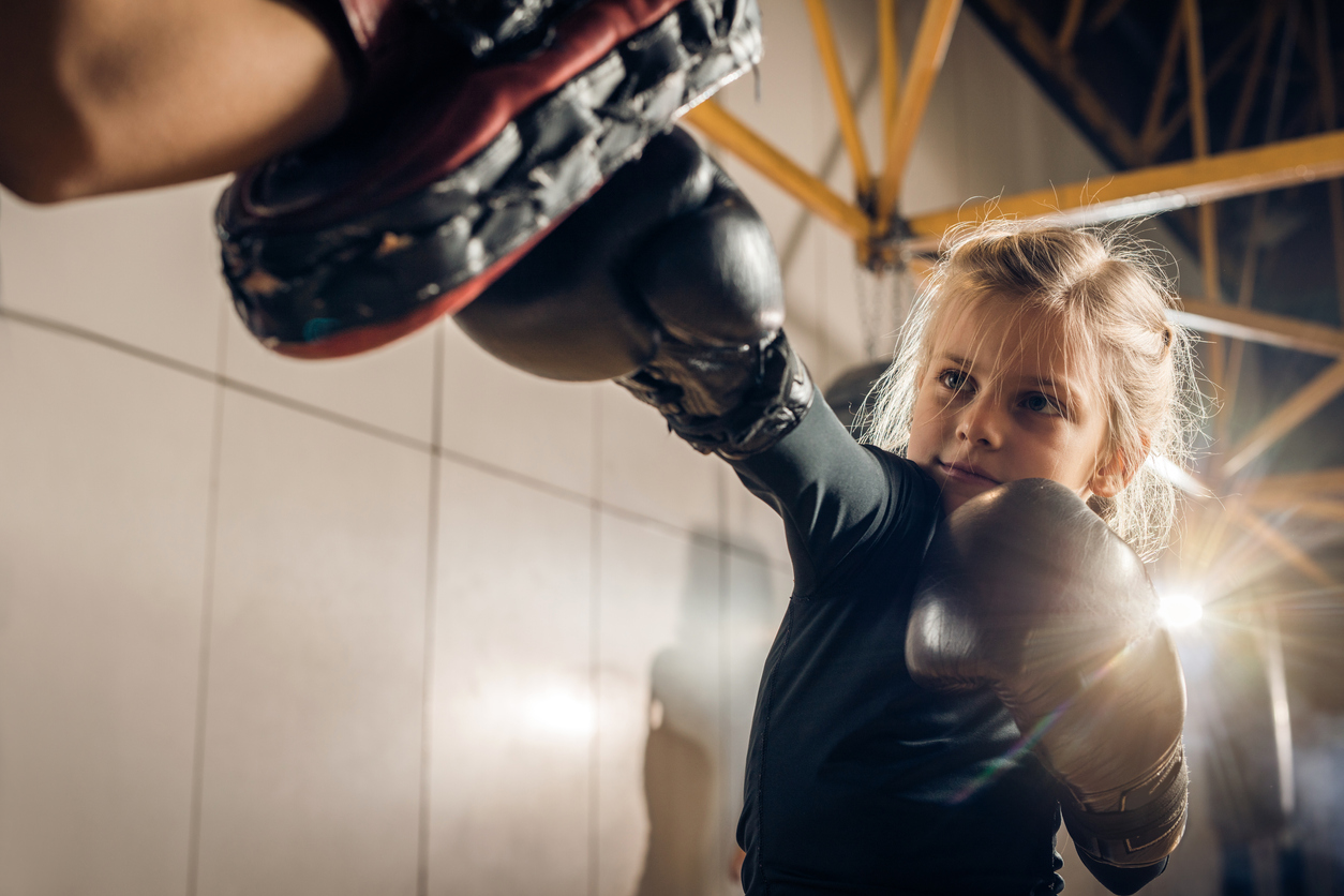 Small girl punching boxing mitt with coach.